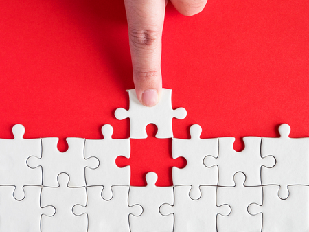 Woman use finger to fill white jigsaw puzzle on red background in top view (Business Concept)の写真素材