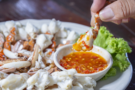 Close up of holding steamed crab in hand over spicy seafood sauce in the restaurant / delicious seafood in Thailand (Selective Focus)の写真素材
