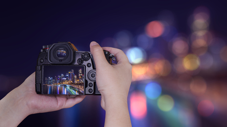 Woman photographer hold digital camera to take photo with bokeh background of cityscape night light...
