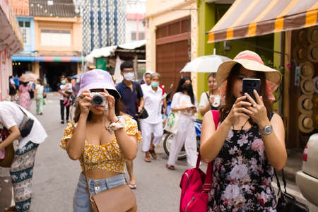 Two tourist casual women wear hat taking photo in walking street of Phuket city. One of most popular tourist city in Thailand : 18 October 2020 - Phuket province, Thailand.