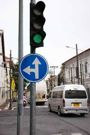 A green traffic light with sign board go straight and turn left with cars and city in view behind : 18 October 2020 - Phuket city, Thailand.のeditorial素材