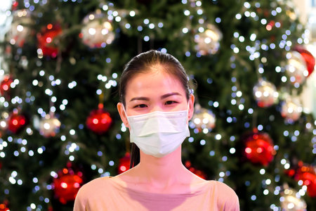 Portrait of young Asia woman wearing sugical mask at christmas tree. Smile. Concept New Year. New beginning. Health protection.の写真素材