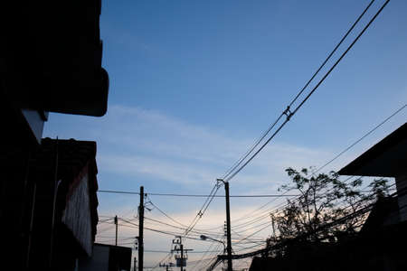 Electric power line pole near by house and village - silhouette in twilight blue sky sunset.