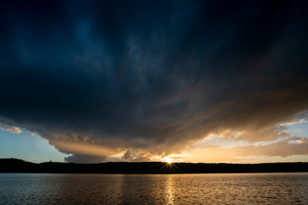 Dramatic sunset over a lake with dark clouds reflected in the waterの写真素材