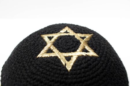 Closeup of a black kippah with a golden david star on top on a white background.