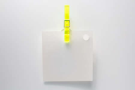 A blank note hanging on a white wall with a yellow clip. Office.の写真素材