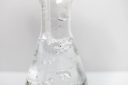 Closeup of a glass erlenmeyer flask with a plastic pipette in it with bubbles in the liquid on a white background. Science.の写真素材
