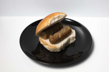 A frikandel sandwich on a black plate with a white background. Dutch snack frikandel.