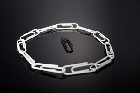 A circle of paperclips with one in the middle that is not fitting in and is surrounded by the others. Symbolic representation of not fitting in the group, being bullied or feeling anxiety. Alone.の写真素材