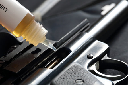 Closeup of a bottle of oil lubricating a pistol. Weapon maintenance, cleaning and lubricating. CLP...