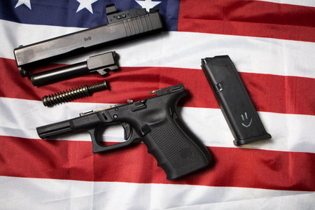 Closeup of a disassembled pistol on the American flag. Gun laws in the USA. Handgun parts. Top view disassembly weapon, weapon maintenance.の写真素材