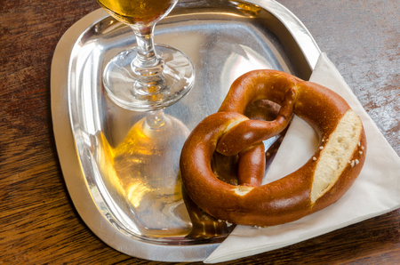 pretzel on a shiny metal tray with the reflection of the beer glass