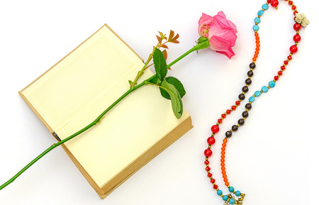 pink rose on a blank page of an old book with a colorful necklaceの写真素材