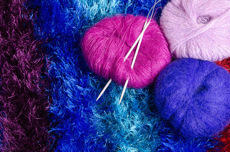 close-up of three flat yarn balls with knitting needles on colorful blanketの写真素材