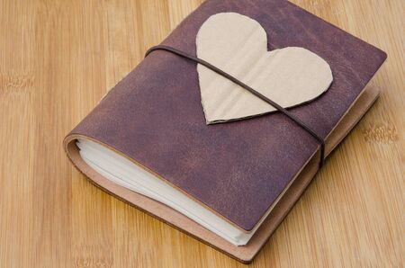 closeup of an old notebook with a cardboard heart on top on a wooden tableの写真素材