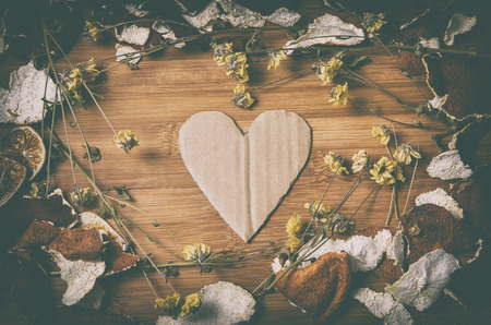 cardboard heart surrounded by a frame of dry citrus peel and withered flowers on a wooden table in vintage lookの写真素材