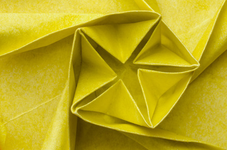 Abstract closeup of an intricate spiral shaped yellow paper origami flower. Top view.