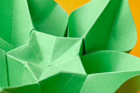 Abstract closeup of a green paper origami flower with star shape in the middle on orange background. Side view.の写真素材