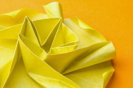 Abstract closeup of an intricate spiral shaped yellow paper origami flower on orange background. Side view.の写真素材