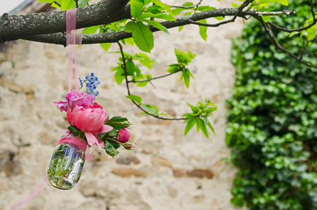 decorative improvised glass flower pot hanging from a tree in front of an old stone wall in a parkの写真素材