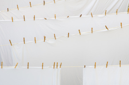 background of many freshly washed white bed sheet layers drying outside on ropes with wooden pinsの写真素材