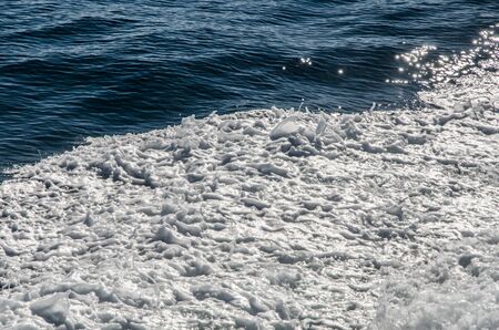 white foam forming on an active sea water surface sparkling on a sunny dayの写真素材