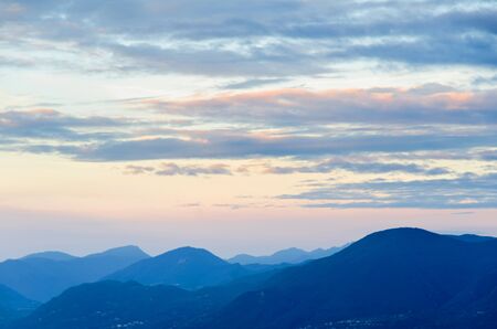 mountains at Lake Garda in Italy in the blue hour of the morning with the clouds above illuminated by the rising sun at dawnの写真素材