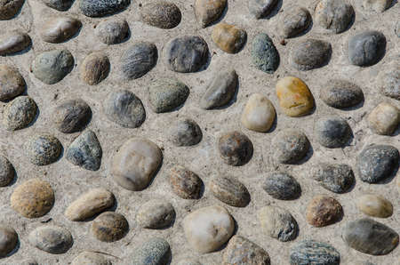 close-up of round colorful rocks in the cement ground on a sunny dayの写真素材