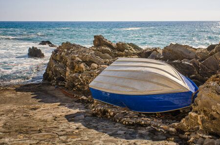A boat resting on the rocks at the coast of Mediterranean Sea in Genoa Nervi, Italyの写真素材