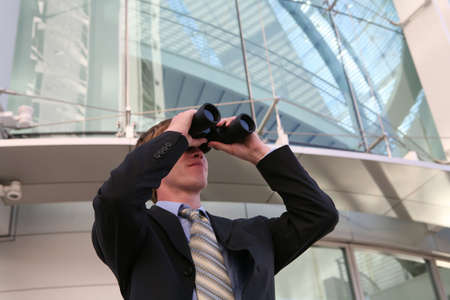 A business man looking into binoculars at his companyの写真素材