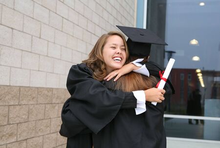 Two students celebrating their graduation with a hugの写真素材