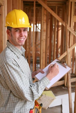 A handsome construction worker with a clipboard at a home building site