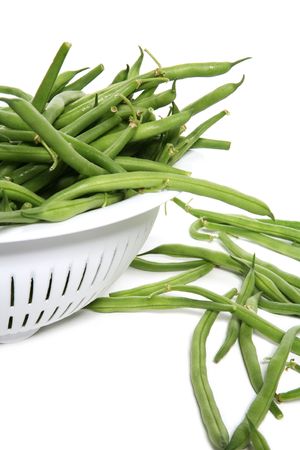 Fresh green beans in a strainer over white