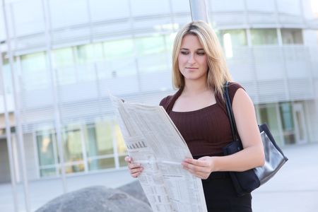 A pretty business woman reading the newspaper outside her company の写真素材