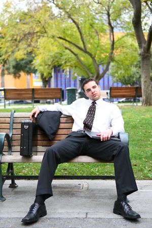 A handsome bored business man resting on bench outside officeの写真素材