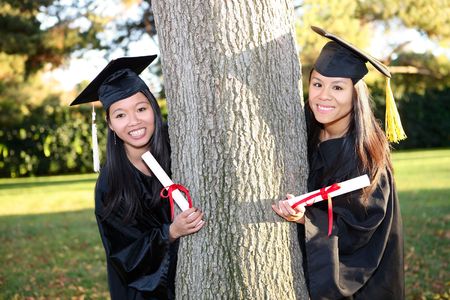 Pretty Asian woman wearing cap and gown holding diploma at graduationの写真素材