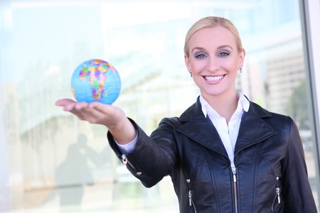 A beautiful young blonde woman holding a globe at office buildingの写真素材