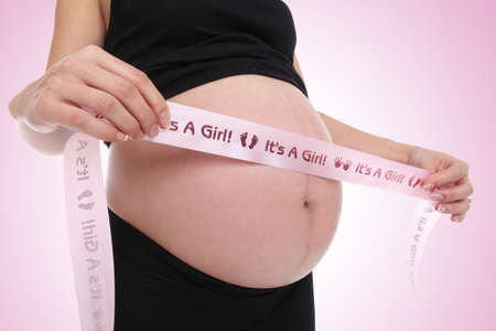 A pregnant woman with an its a girl ribbon around stomachの写真素材