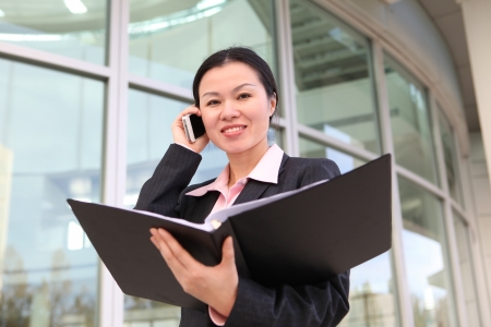 A pretty Chinese business woman smiling outside office building on phoneの写真素材