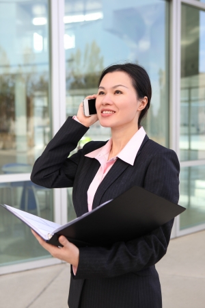 A pretty Chinese business woman smiling outside office building on phoneの写真素材