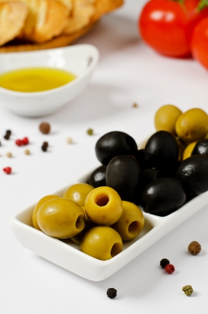 Green and Black olives with olive oil and tomatoes in the backgroundの写真素材