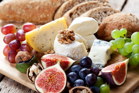 Cheese platter: variety of cheeses on wooden plate with fruits and breadの写真素材