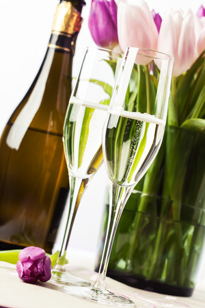 Two champagne flutes and a bottle of sparkling wine with tulips on backgroundの写真素材
