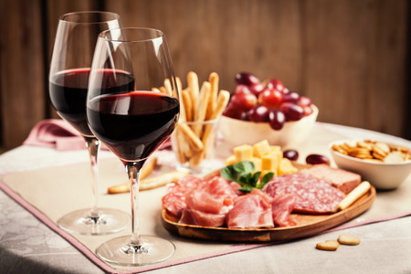 Two glasses of red wine with charcuterie, cheese, grapes and snacks