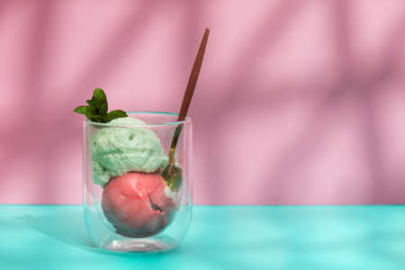 Raspberry and pistachio ice cream scoops in glass on pastel colored backgroundの写真素材