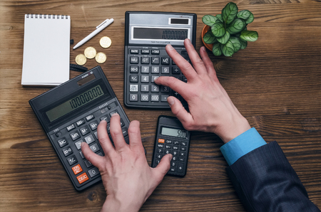 Tax inspector or banker desk table background. Businessman male hands, notepad and calculator on wooden table top view.の写真素材