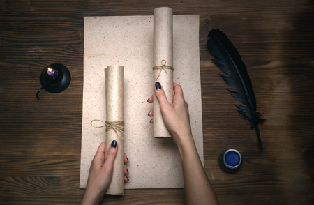 Woman holding in hands a secret documents scrolls and stretches them forward on wooden table background. Agreement conclusion. Contract.の写真素材