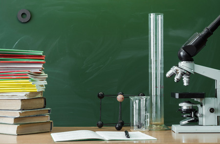 Teacher, student, biologist or chemist desk table. Education background. Education concept. Microscope, vial, flask, beaker, stacked books and copybook book with pen on the table.の写真素材