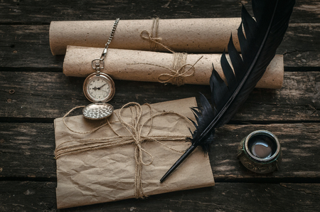 Old vintage letter envelope, feather pen and inkwell on aged wooden table board background.の写真素材