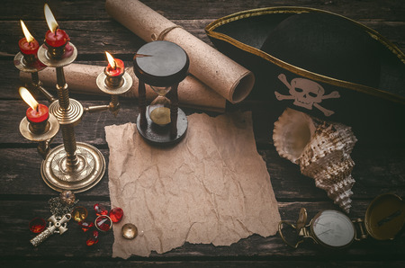 Pirate captain table with crumpled paper page with copy space for treasure map, golden compass, sand watch, scrolls,gemstones and seashell.の写真素材